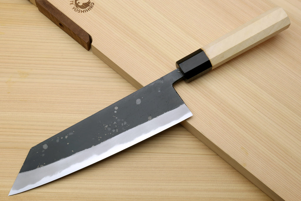 Kiritsuke chef knife with speckled dark blade, black handle, and light wood saya