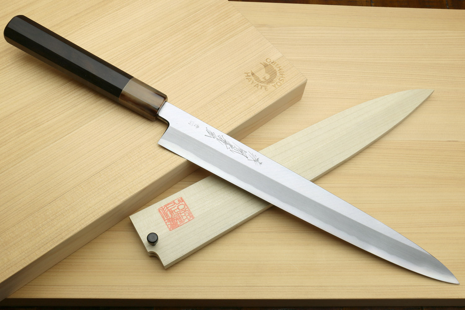 Yanagi sushi knife with white blade, dark handle, and wooden saya
