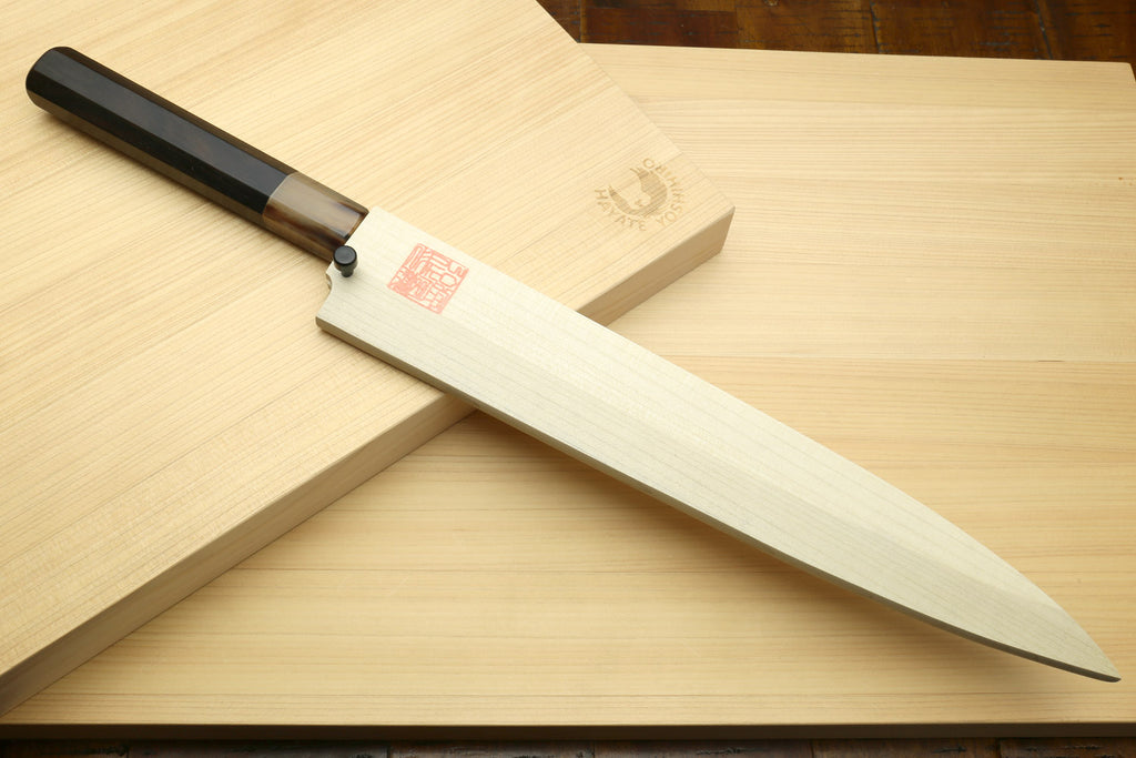 Yanagi sushi knife on wooden board with saya and dark handle