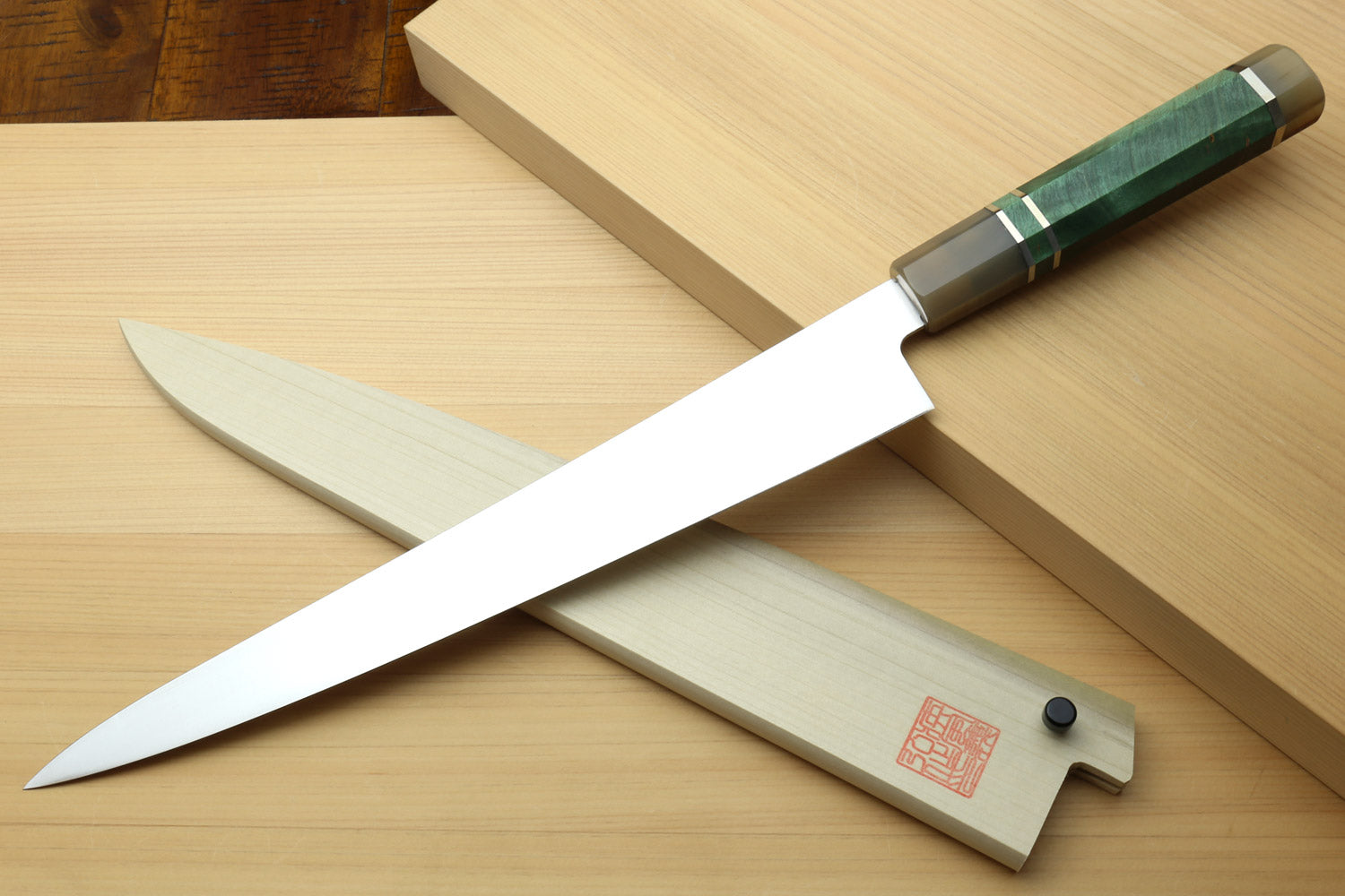 Sujihiki slicer knife with long white blade and dark green handle, beside wooden saya