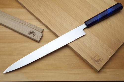 Yanagi sushi knife angled on board, white blade with dark-blue handle and saya