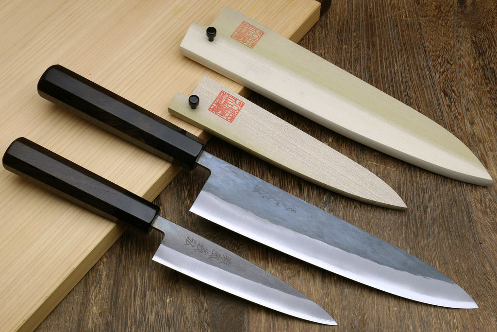 Two kitchen knives with black handles and silver stainless blades on a wooden surface.