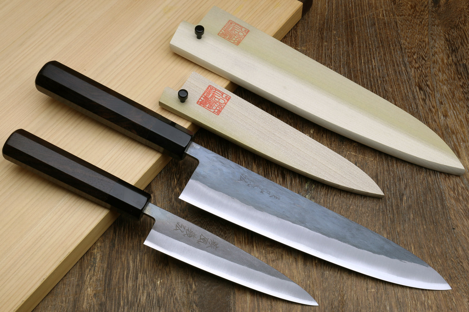 Two kitchen knives with black handles and silver stainless blades on a wooden surface.