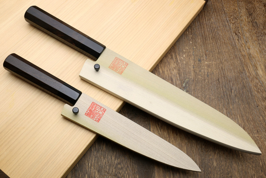 Two kitchen knives with black handles and silver stainless blades, laid on wood.