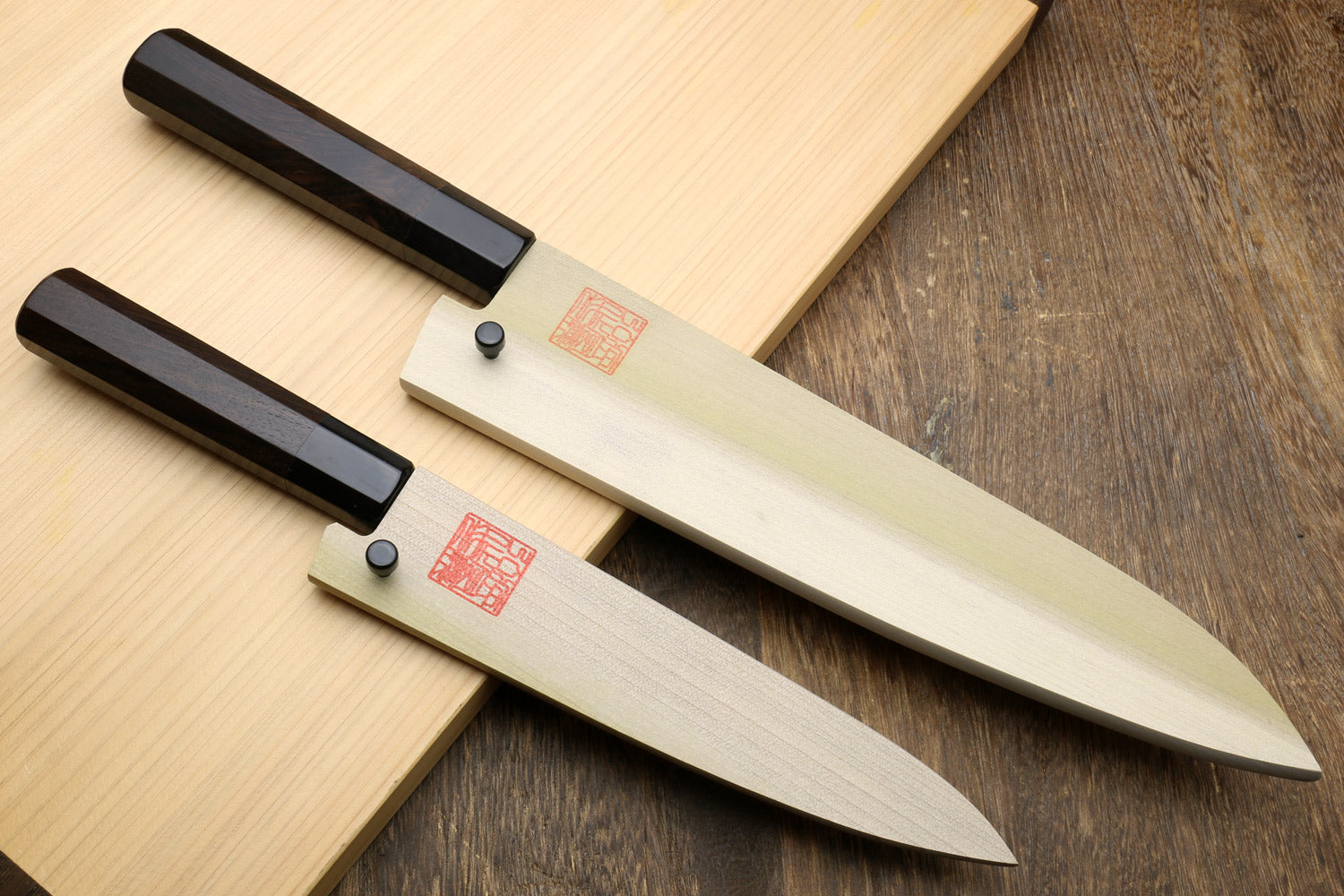 Two kitchen knives with black handles and silver stainless blades, laid on wood.