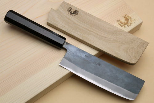 Nakiri knife with black handle and blue-steel blade resting on wooden saya cover