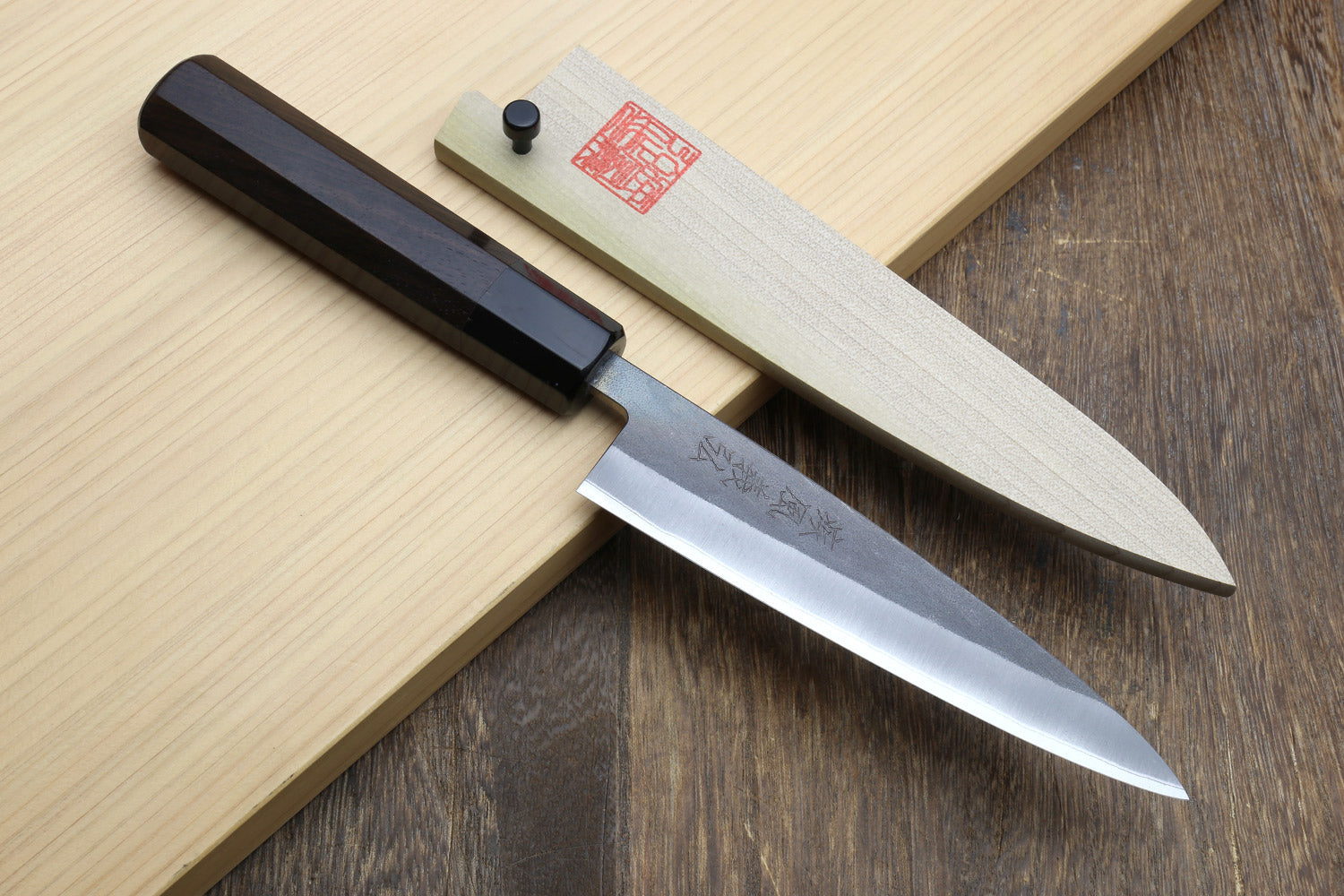 Petty utility knife with dark ebony handle and stainless blade, on wood board