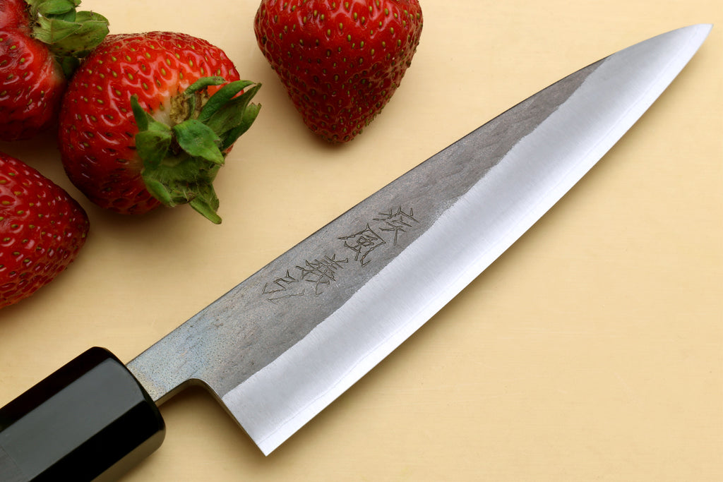 Petty utility knife with dark ebony handle and stainless blade edge, close-up angle