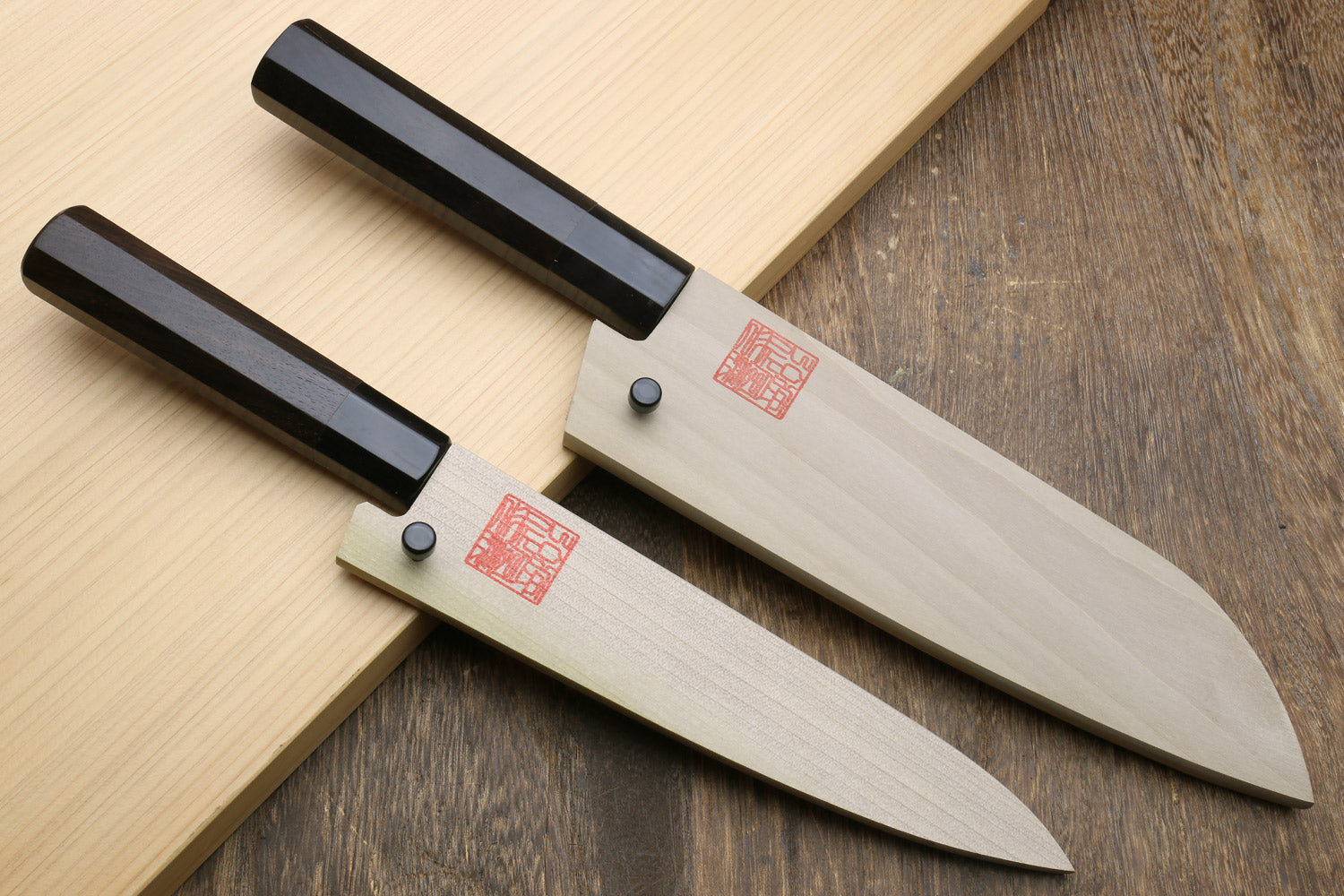 Santoku and petty knives with black handles and stainless blades on wooden board