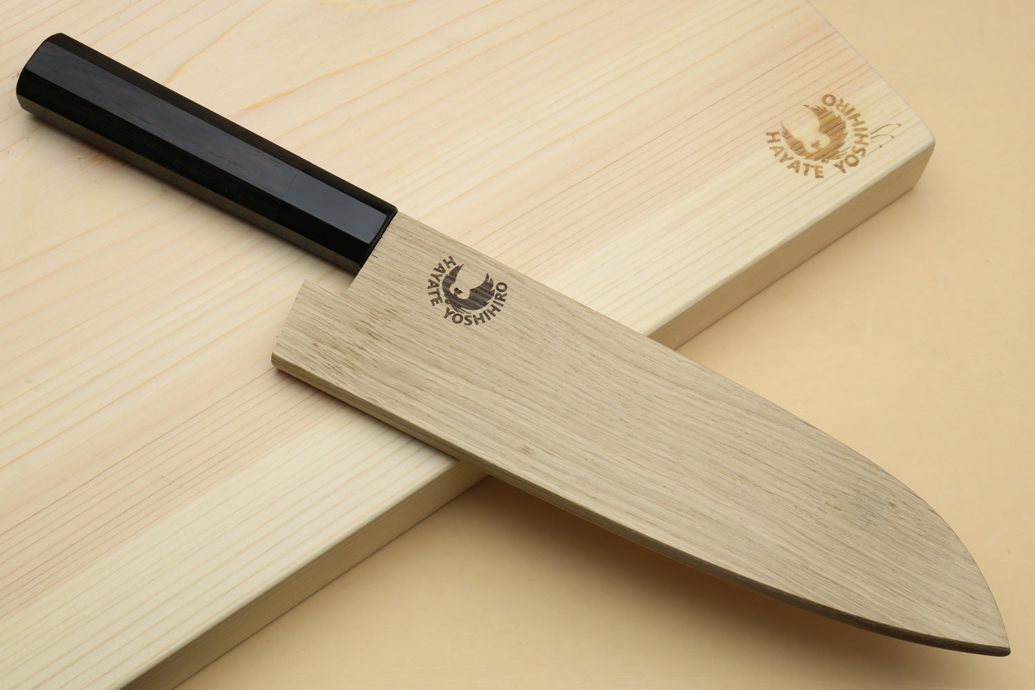 Santoku knife with ebony handle and saya-style wooden cover, top angle on board