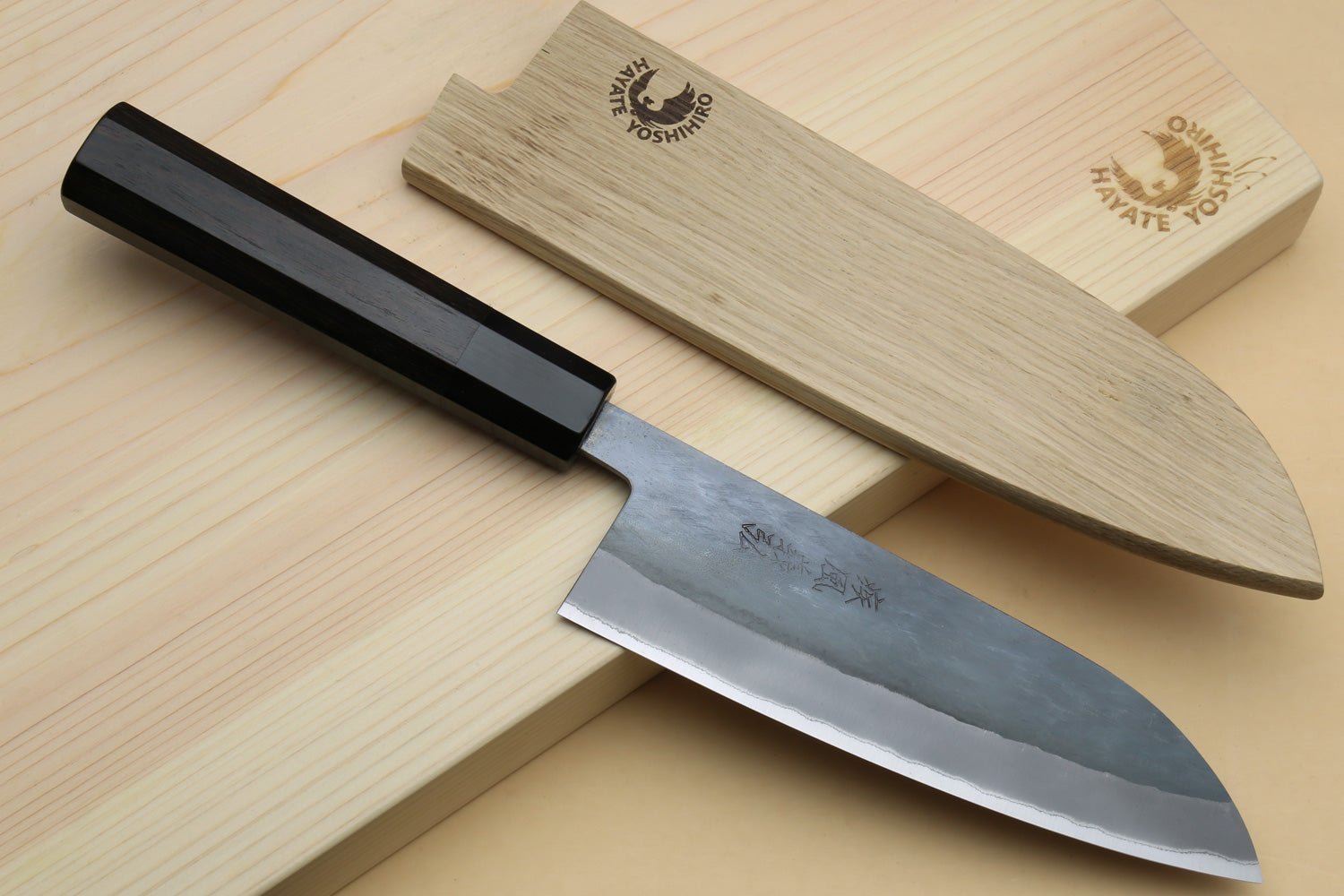 Santoku knife with ebony handle and saya-style wooden cover on light wood board