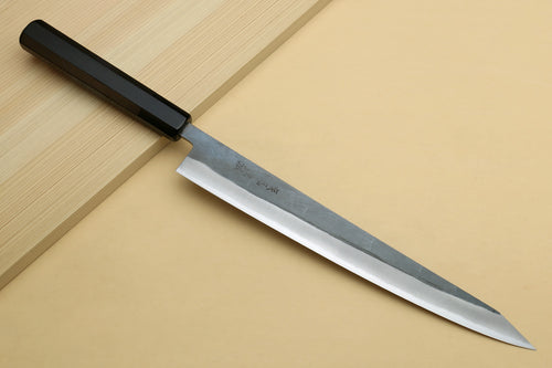 Sujihiki slicer knife with silver blade and dark ebony handle laid across boards.