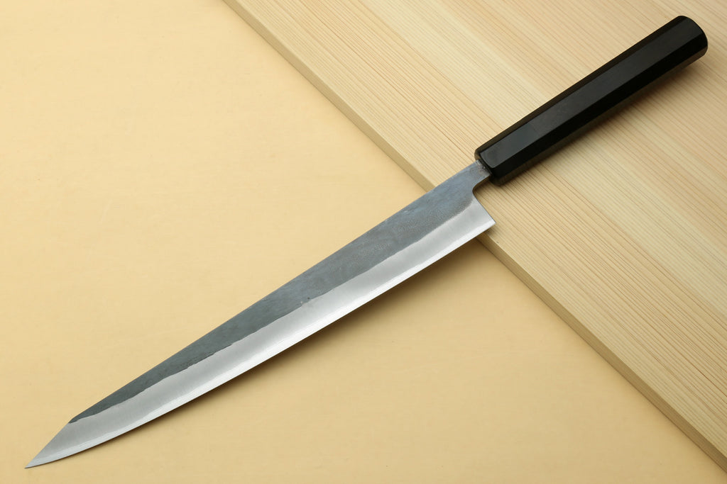 Sujihiki slicer knife with silver steel blade and dark ebony handle on cutting boards.