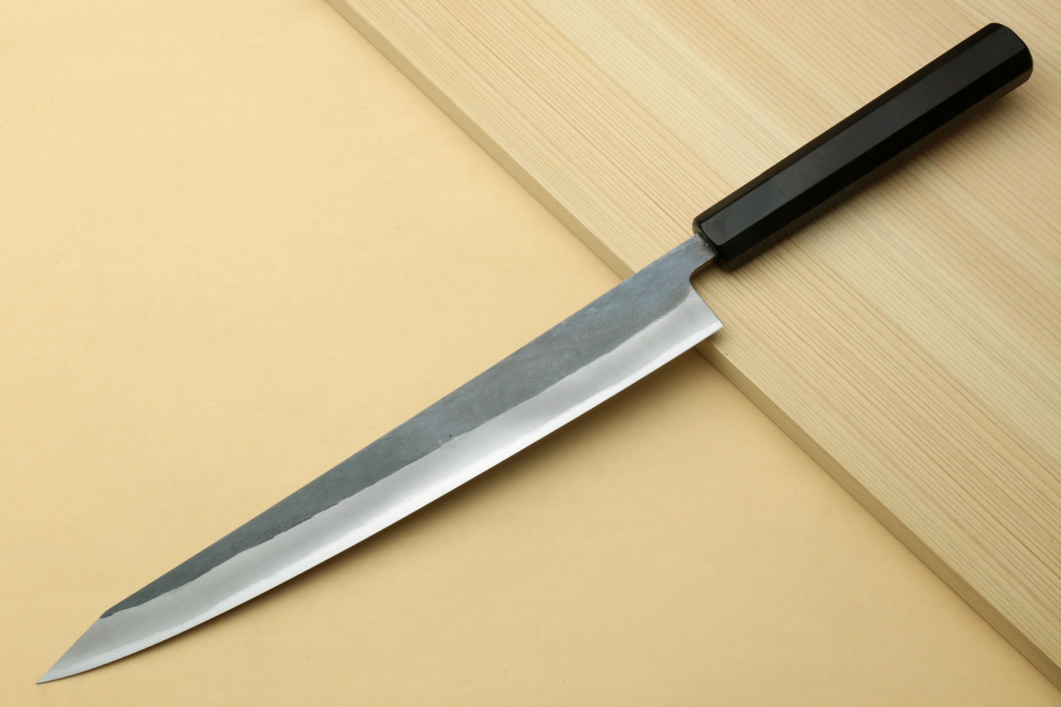 Sujihiki slicer knife with silver steel blade and dark ebony handle on cutting boards.