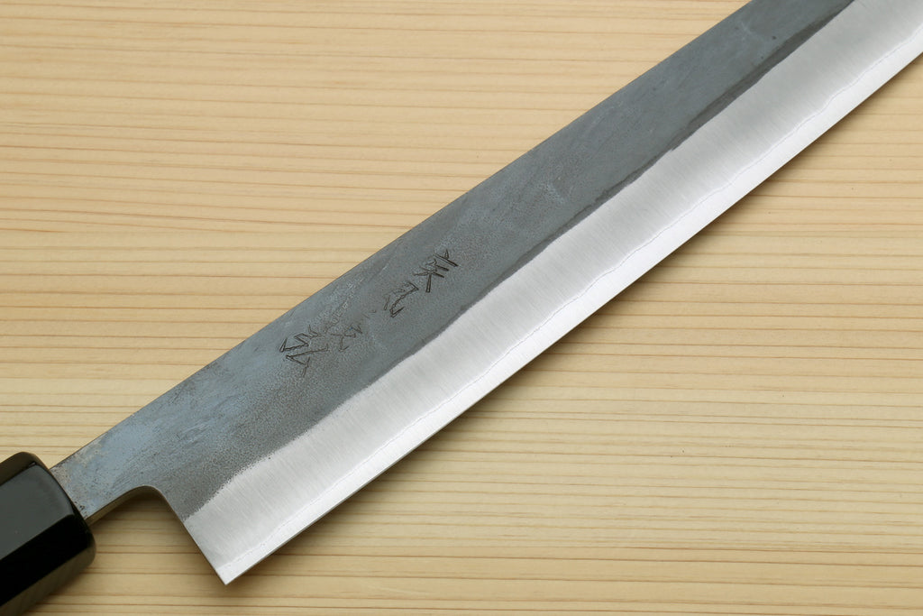 Kiritsuke slicer knife blade close-up with etched markings and dark handle base.