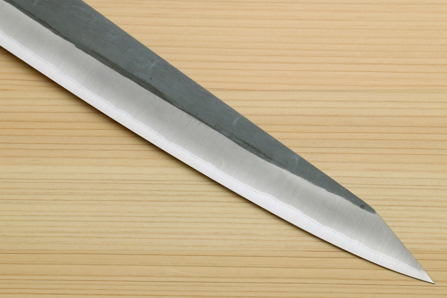 Sujihiki slicer knife with long silver blade and narrow pointed tip; dark handle partial.