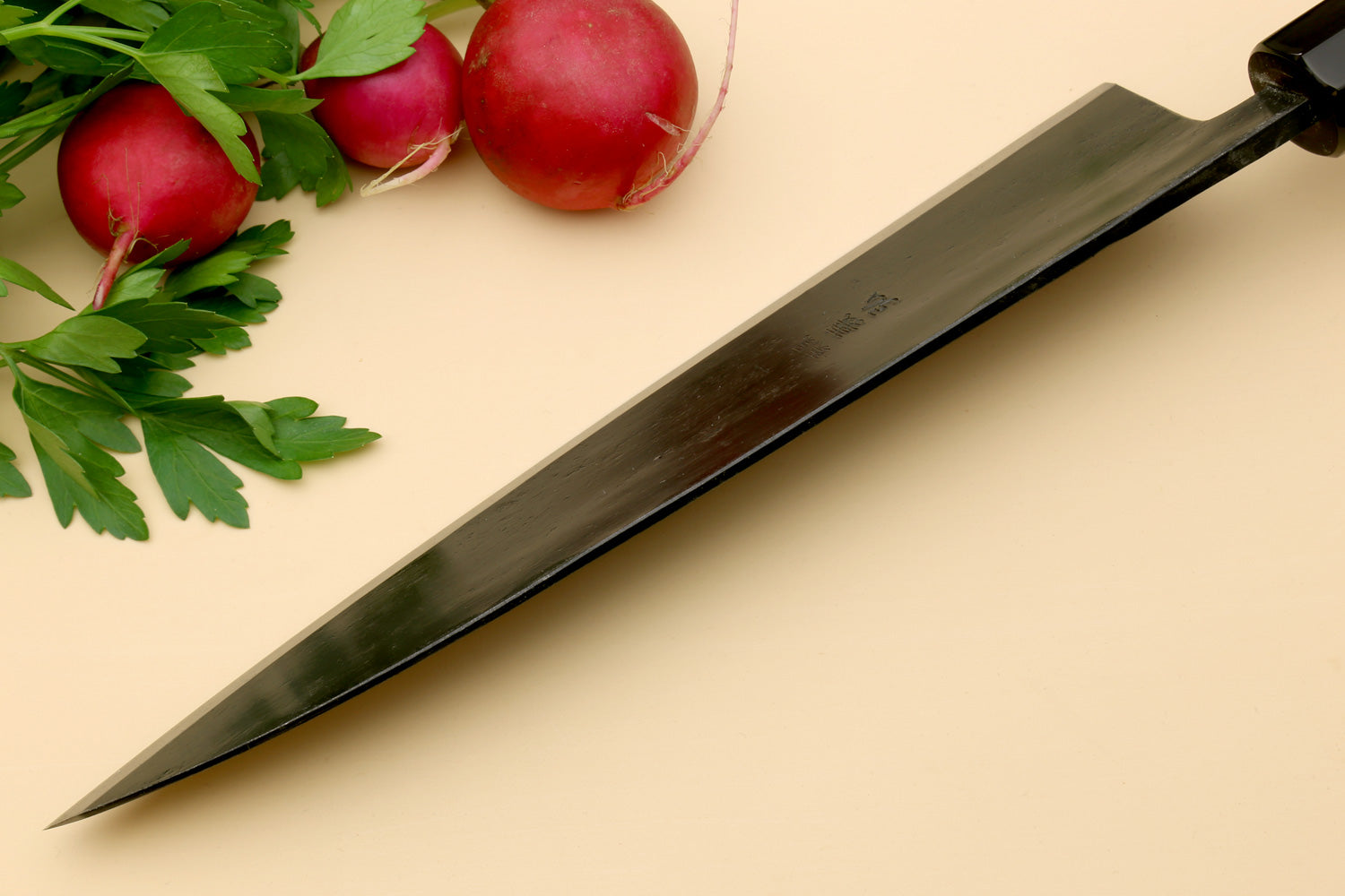 Gyuto chef knife side view with dark blade and pale camphor wood handle
