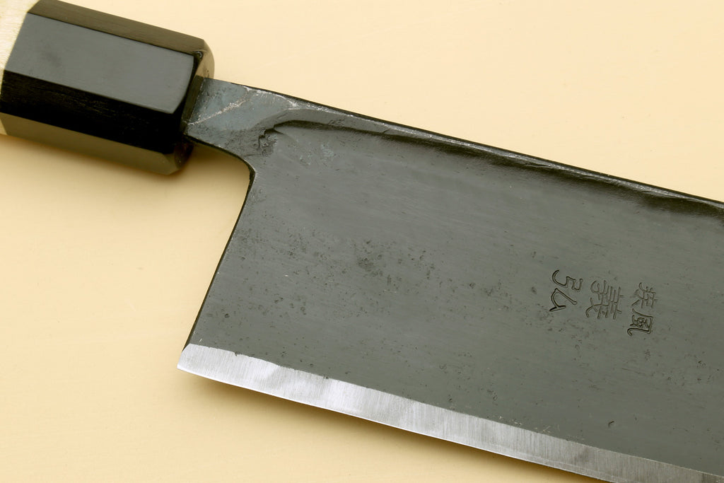 Nakiri vegetable knife close-up: dark steel blade with etched markings, black bolster