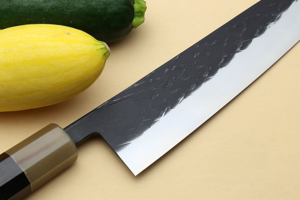 Gyuto chef's knife close-up: black-patterned blade with stainless edge, dark bolster