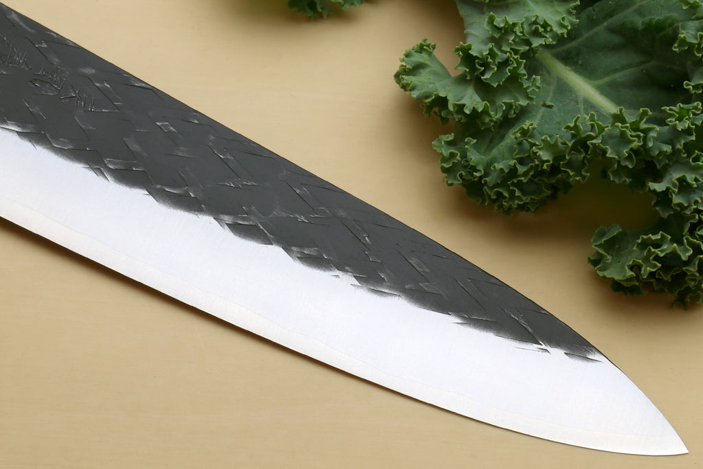 Gyuto chef's knife blade close-up, black-speckled finish and white cutting edge