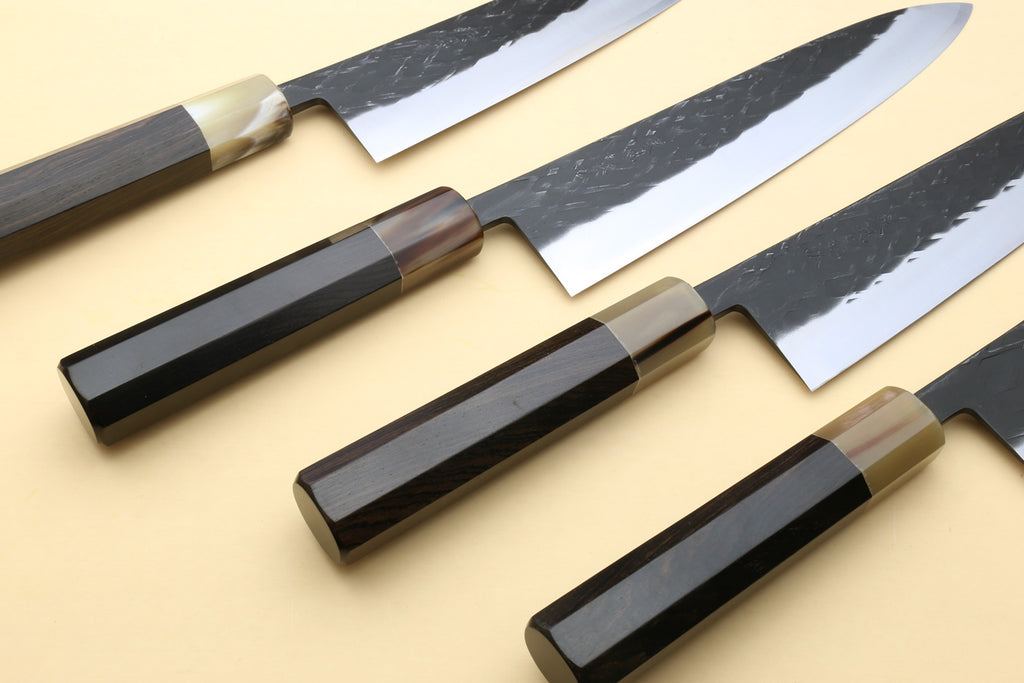 Three Gyuto chef's knives with dark handles and black-speckled blades