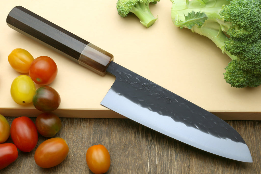 Stainless chef knife with dark handle and speckled blade, shown with mixed vegetables