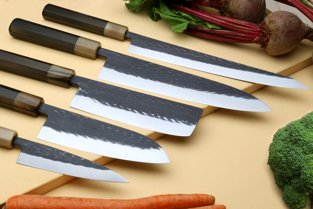 Stainless clad knife set with five blades and dark composite handles on a wooden board