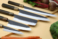 Stainless clad knife set with five blades and dark composite handles on a wooden board