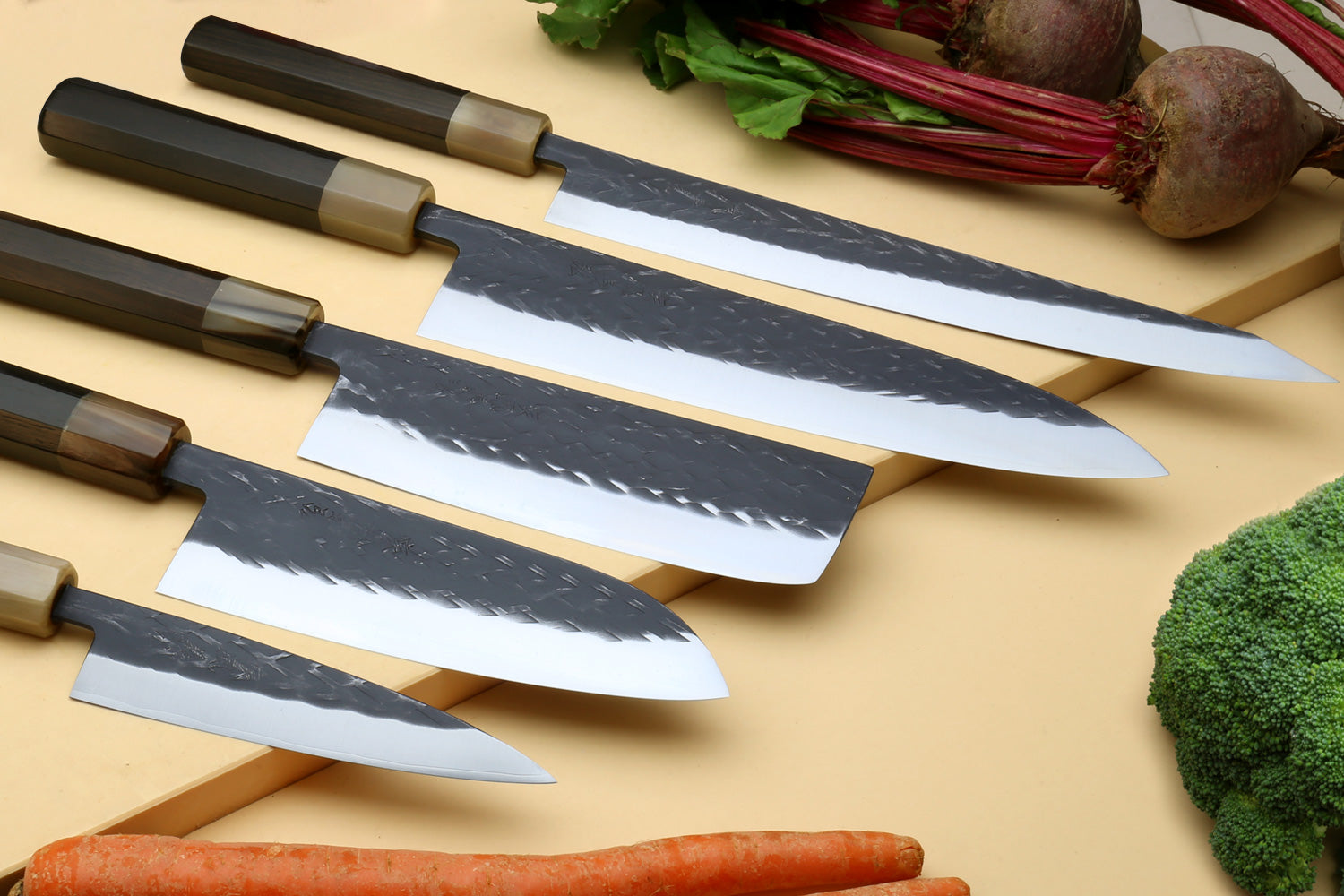 Stainless clad knife set with five blades and dark composite handles on a wooden board