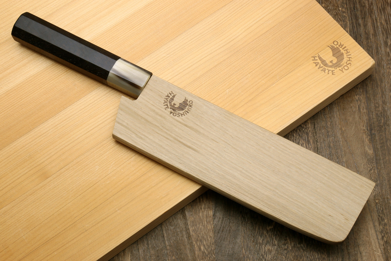 Nakiri vegetable knife with dark hammered blade and black handle, on wooden board