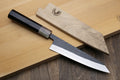 Petty-utility knife with dark handle and wooden saya cover, textured dark blade visible