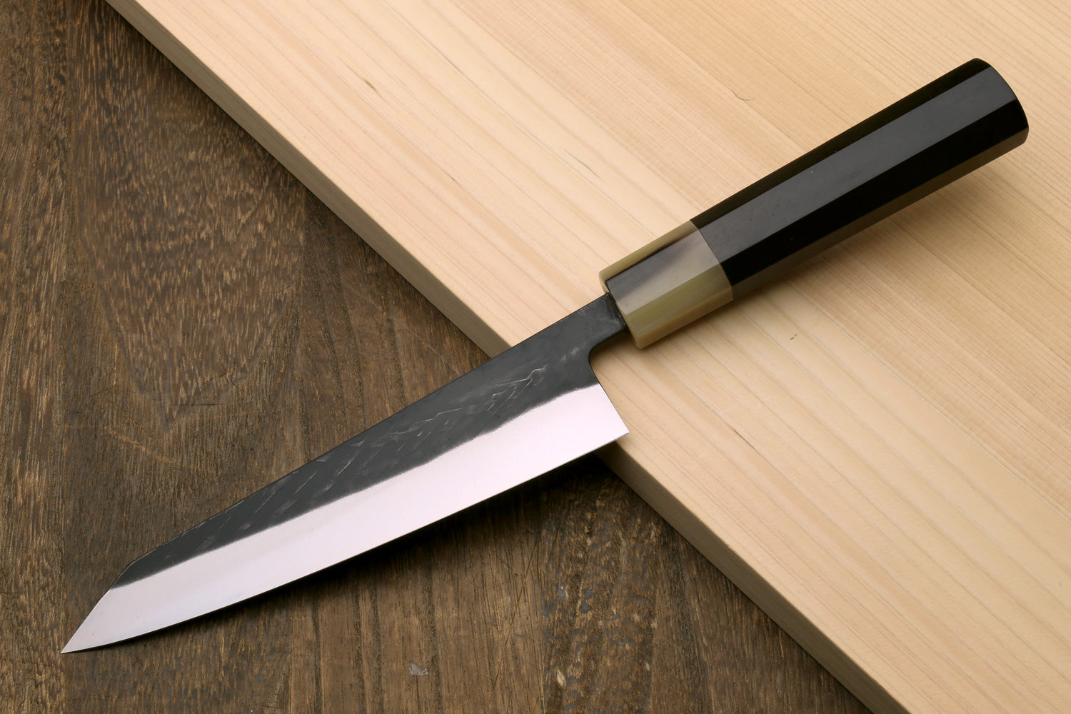 Petty-utility knife with dark handle and textured dark blade, angled view of tip