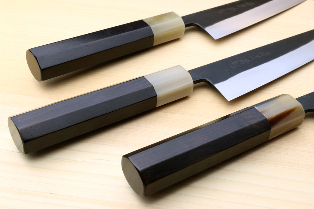 Petty-utility knives laid out: dark handles, light bolsters, and textured dark blades