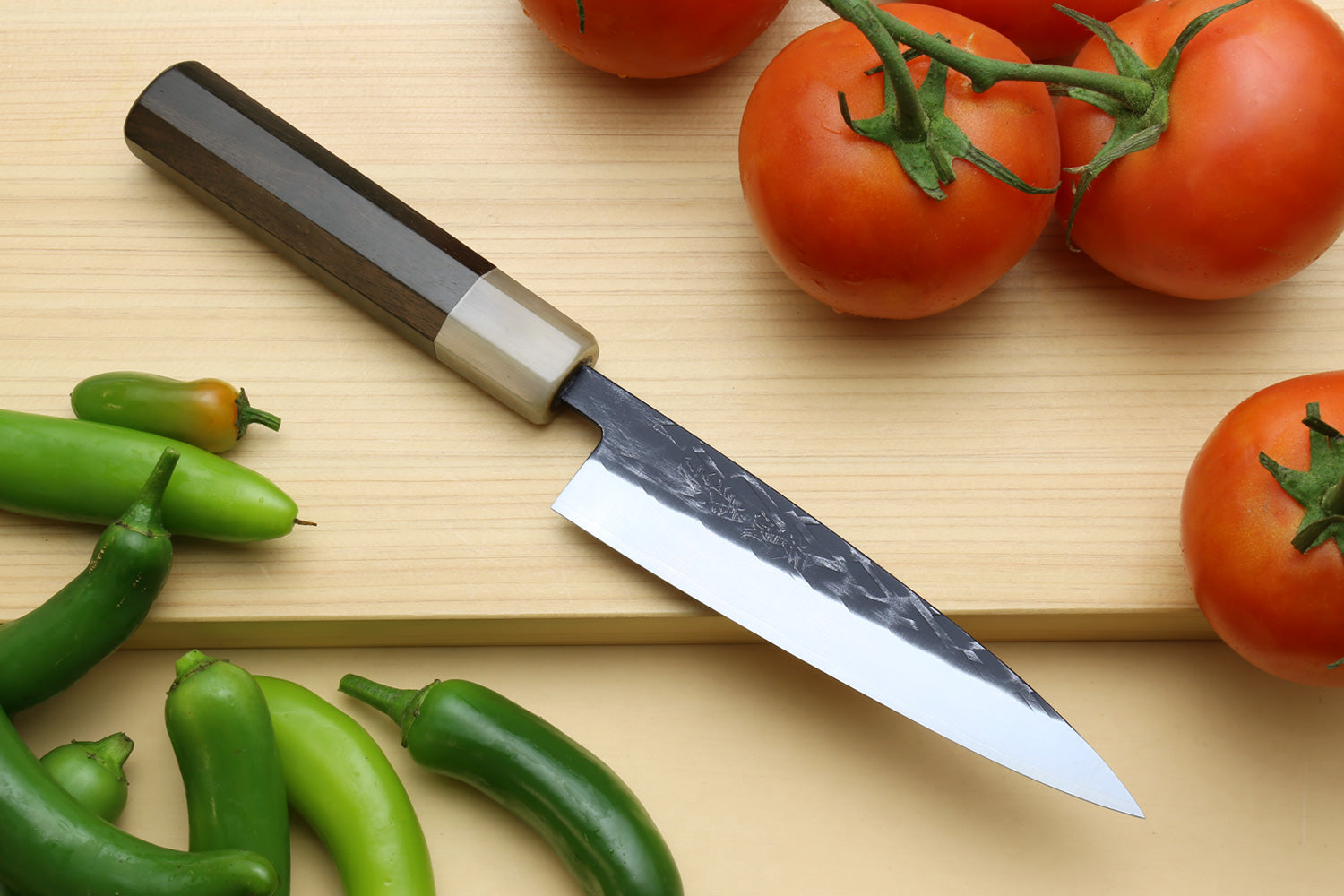 Petty utility knife with black handle and gray patterned blade on wood board