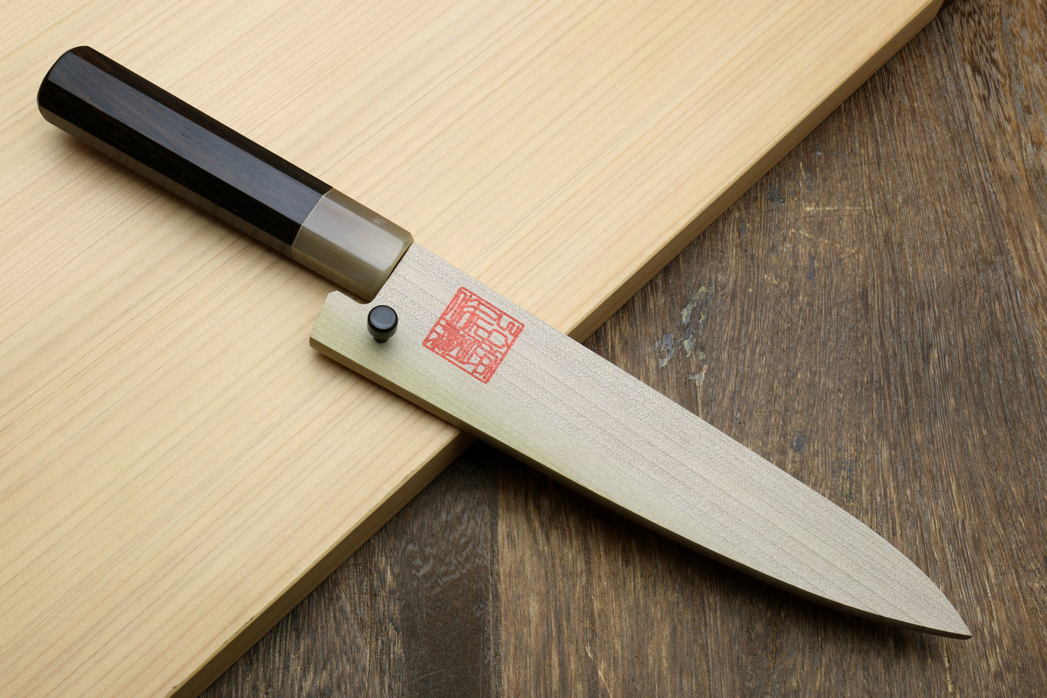 Petty utility knife on wood with black handle, silver bolster, and gray blade