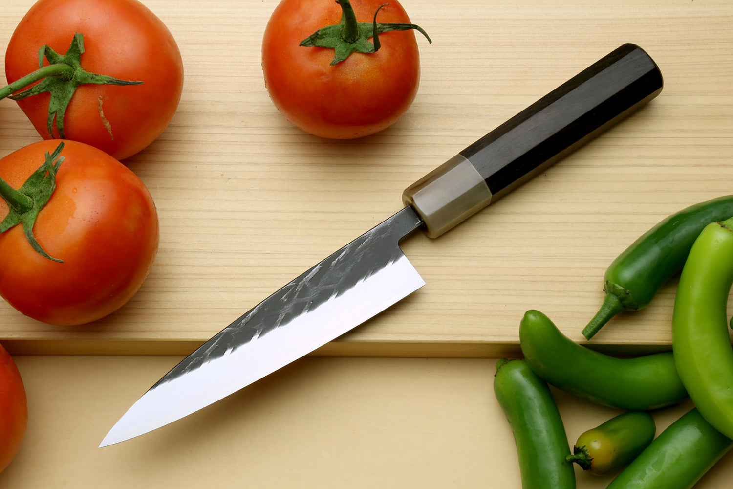 Santoku chef knife with dark handle, bolster, and pointed steel blade