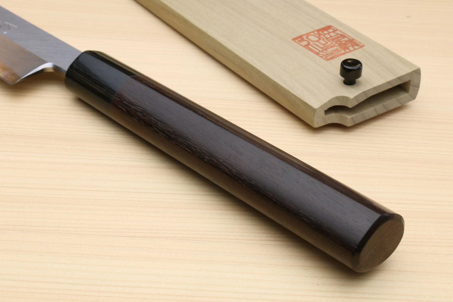 Japanese sushi knife handle made of dark wood with wooden saya shown nearby