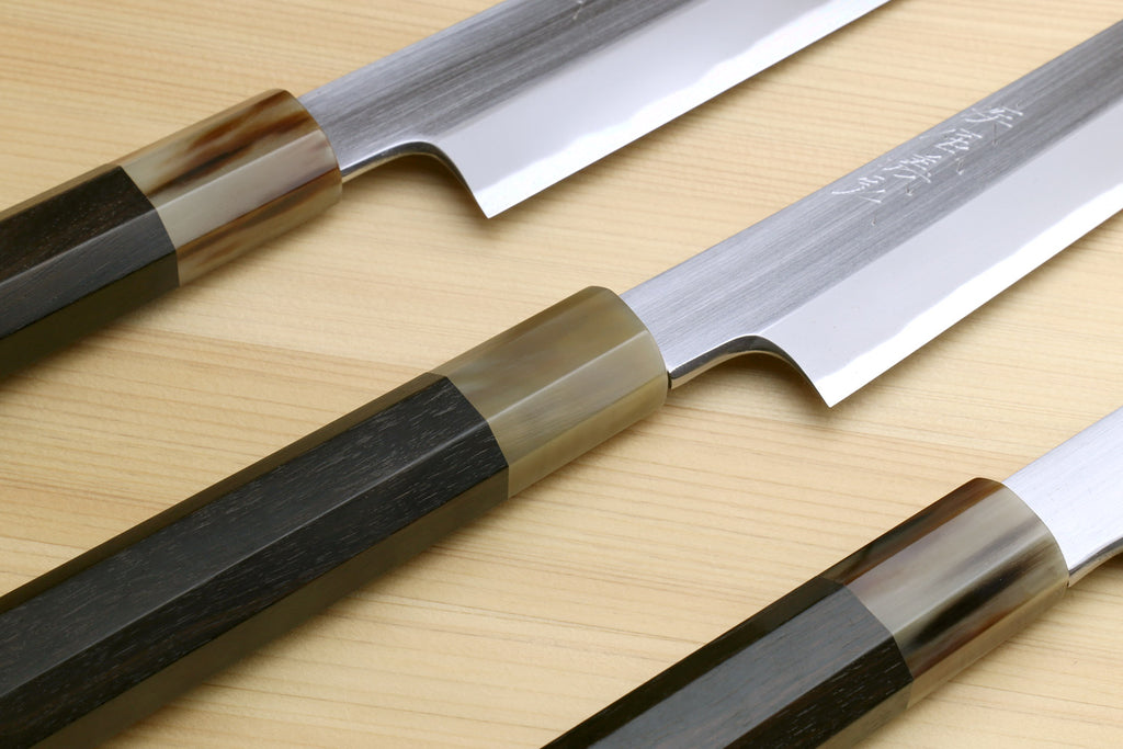 Sushi knives side by side: curved light and dark blades with wood-and-ebony handles