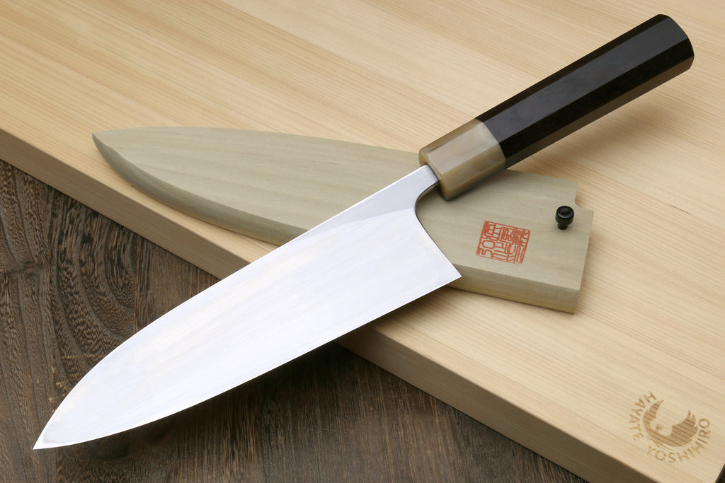 Deba fish fillet knife with white blade and dark handle, angled on light wood