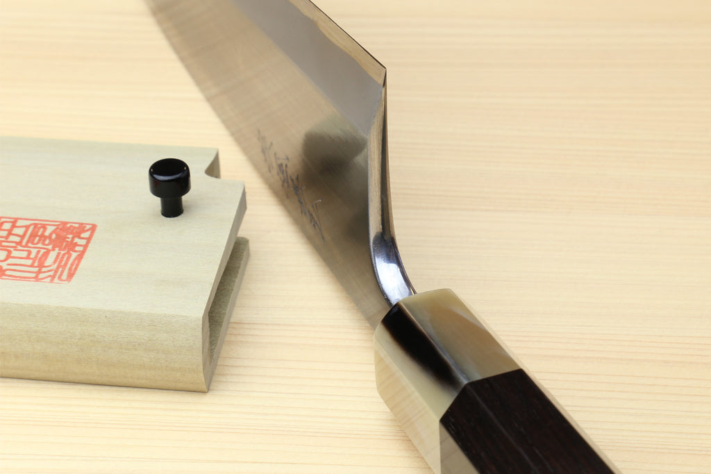 Deba knife side view with white blade and dark handle on wooden block