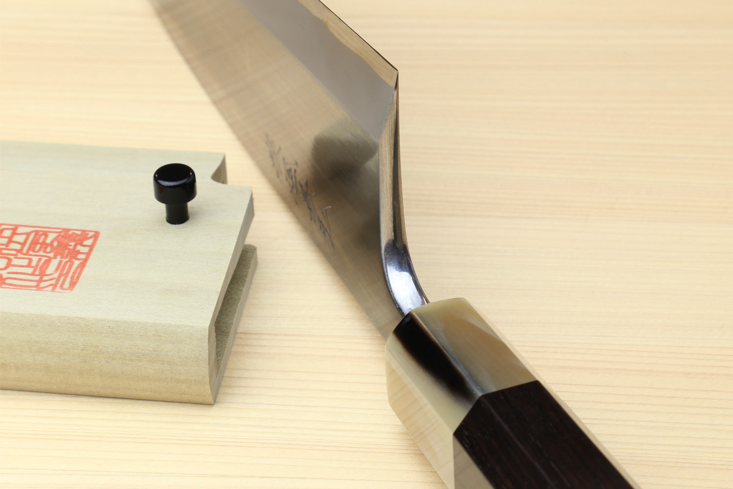 Deba knife side view with white blade and dark handle on wooden block