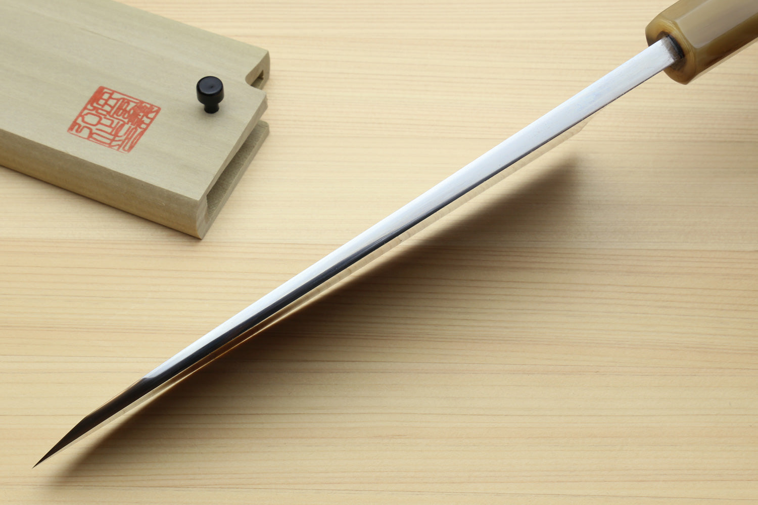 Deba knife with white blade and dark handle, tip pointing left