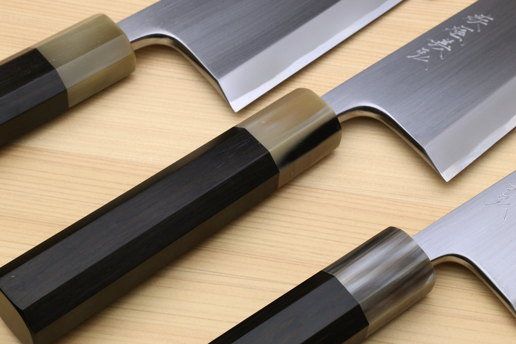 Deba knives with white blades and dark handles, close-up of cutting edges