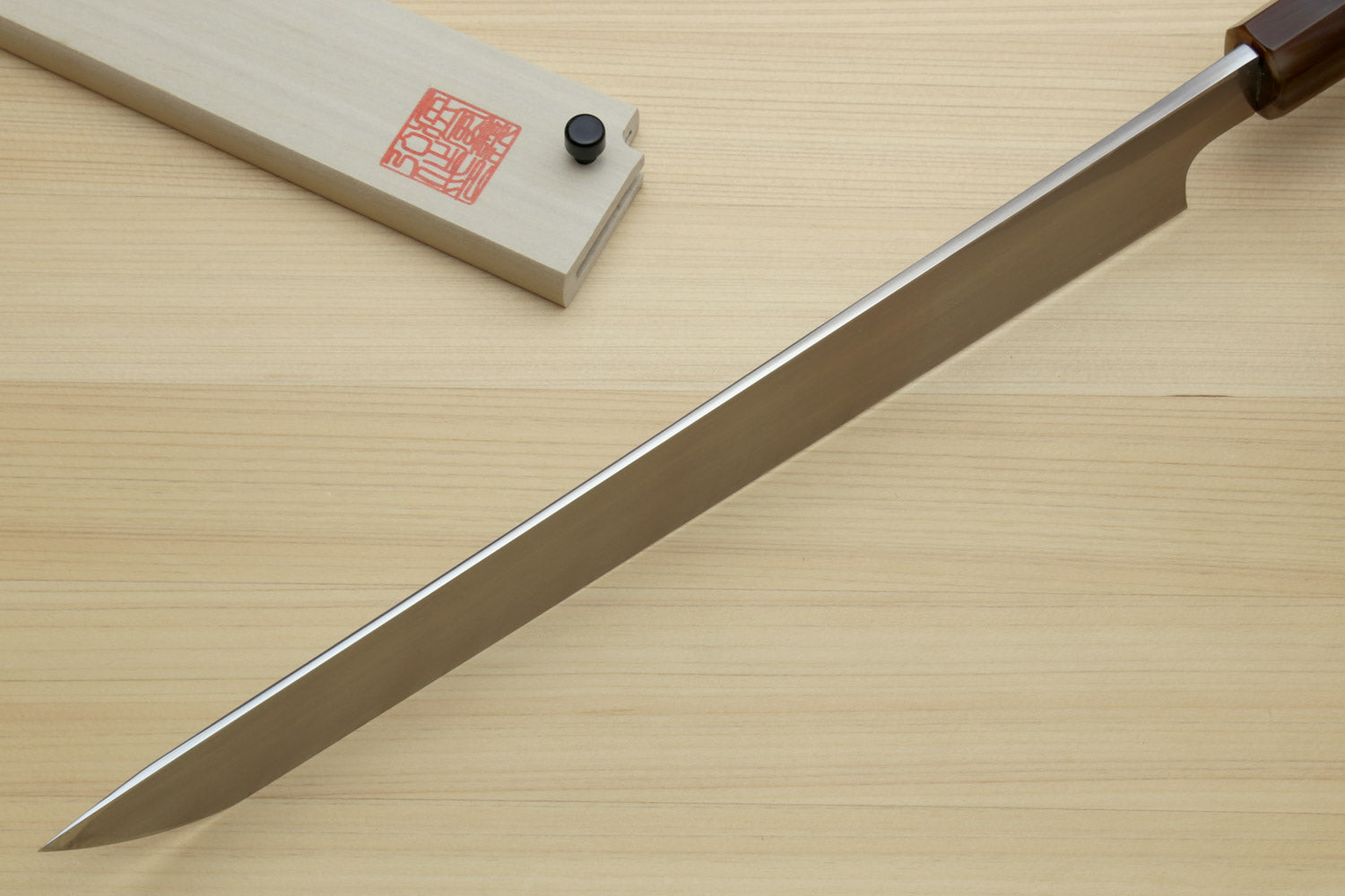 Sashimi sushi knife with long pointed white steel blade and dark handle on wood