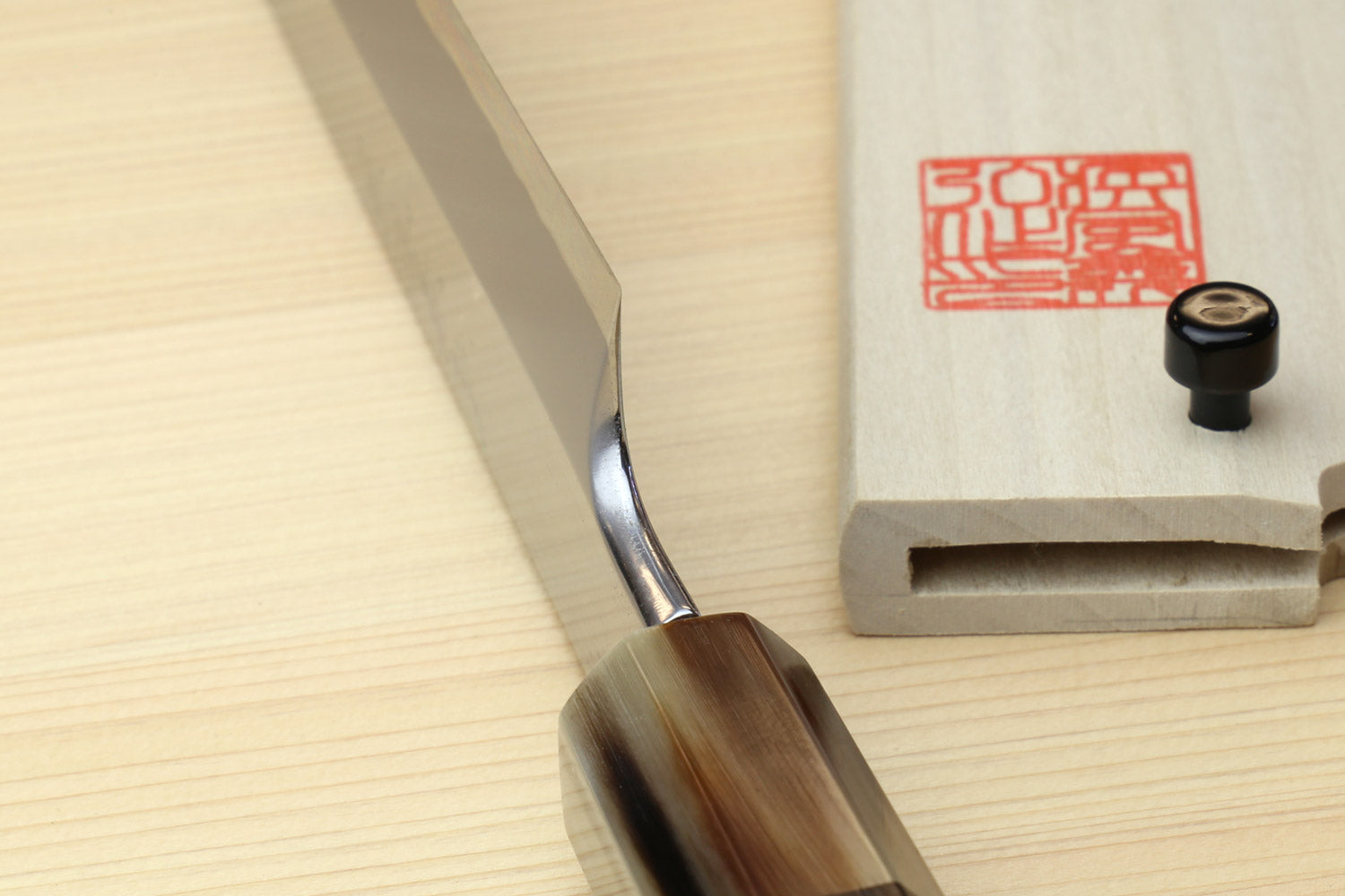 Sashimi sushi knife handle close-up with dark wood grip and wooden saya