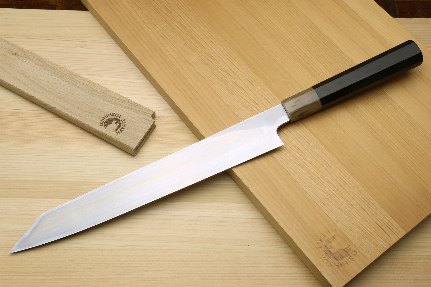 Yanagi-kiritsuke knife with white steel blade and dark handle on wooden boards