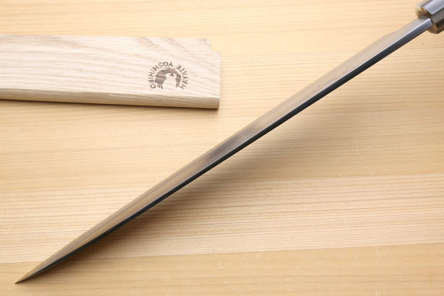 Yanagiba knife with long pointed blade and dark handle on wooden boards