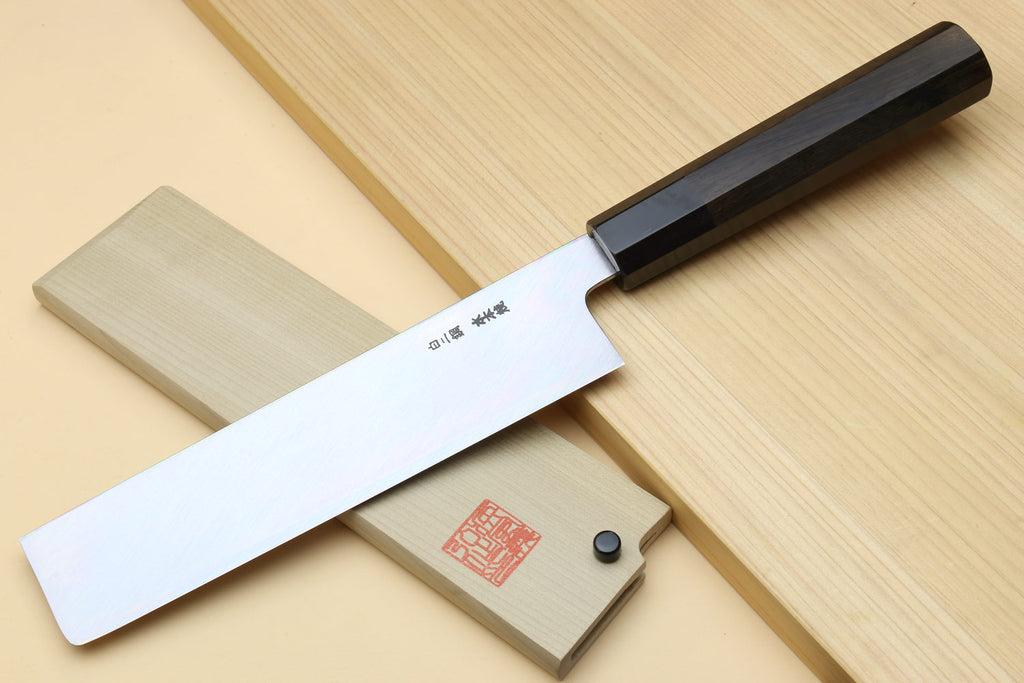 Japanese vegetable knife laid on wood board, white blade with dark spine and ebony handle