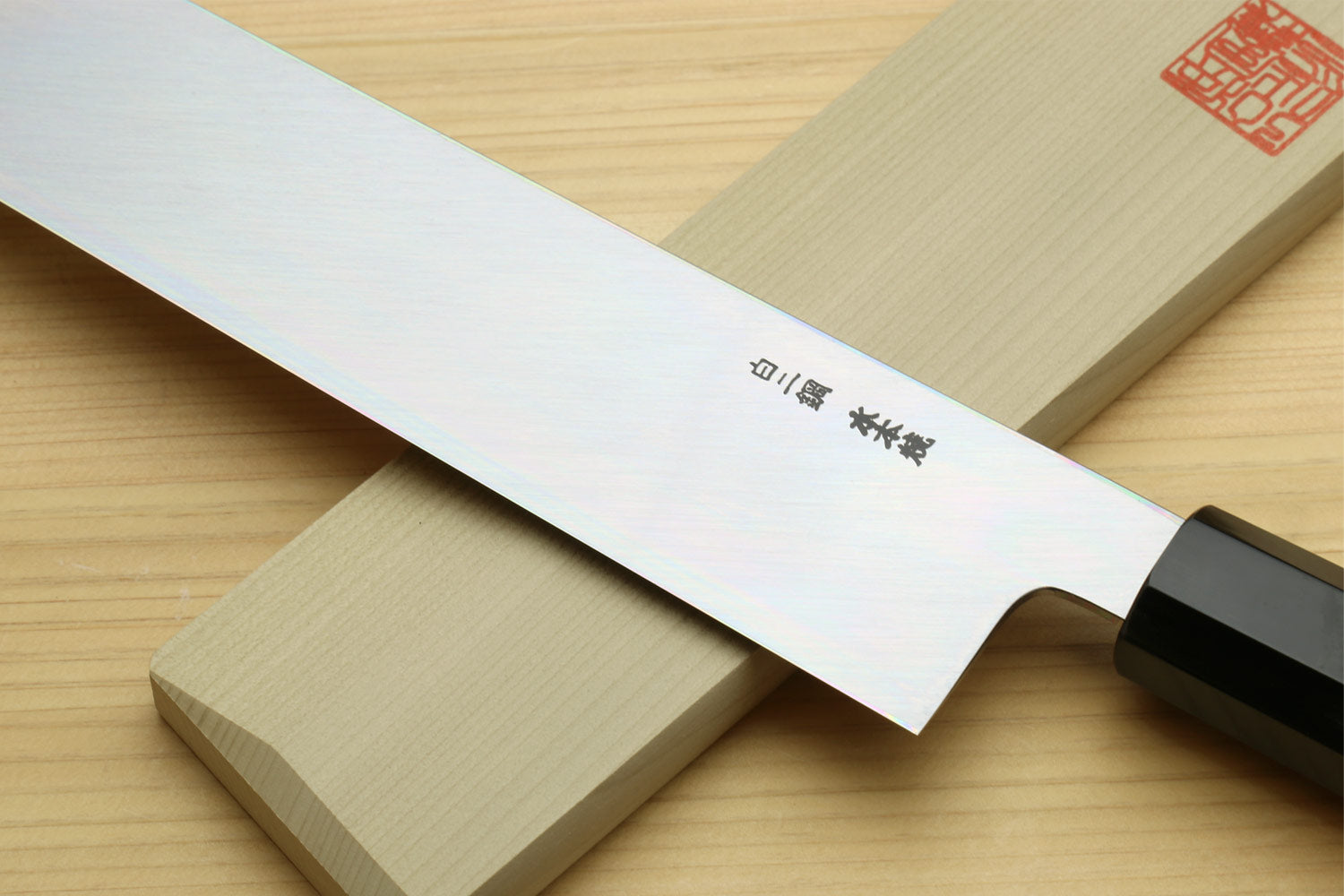 Japanese vegetable knife close-up of white blade edge and dark handle on wood board