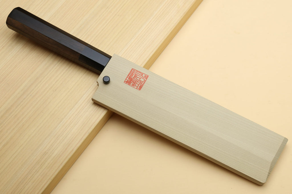 Japanese vegetable knife with white blade and dark handle in sheath-like wooden block